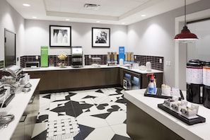 Une cuisine moderne avec un sol à motifs noir et blanc, un coin café et un comptoir où sont disposés divers aliments.