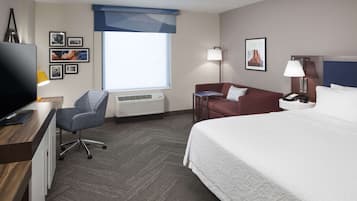 A hotel room with a bed, a desk with a computer, a chair, a couch, a lamp, and a window with a view.
