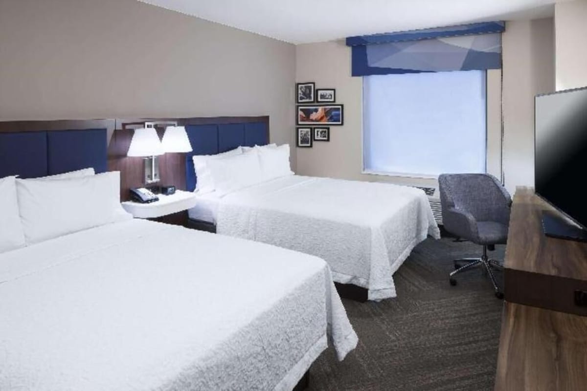 A hotel room with two beds, a desk, a chair, a TV, and a window with a view.
