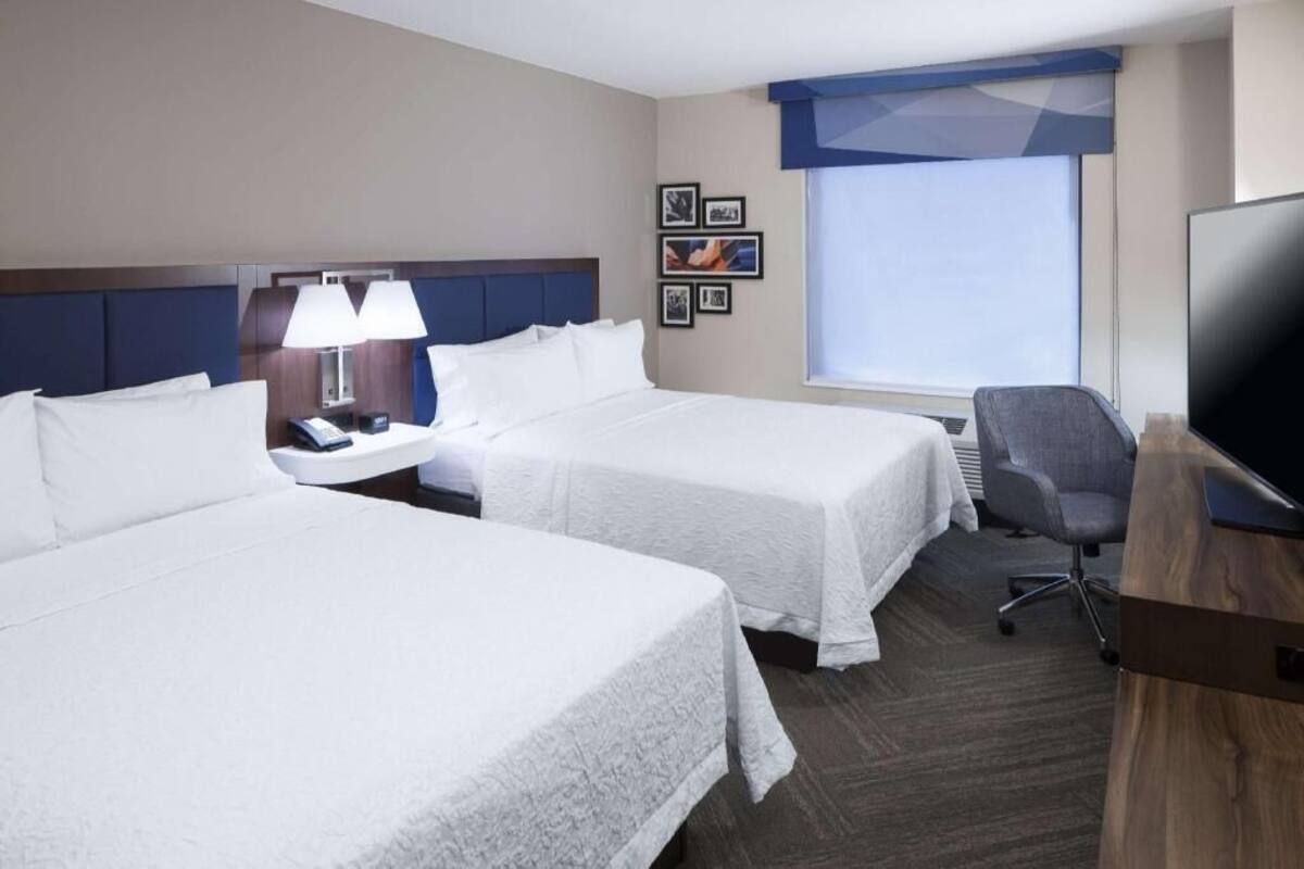 A hotel room with two beds, a desk with a lamp, a television, and framed pictures on the wall.