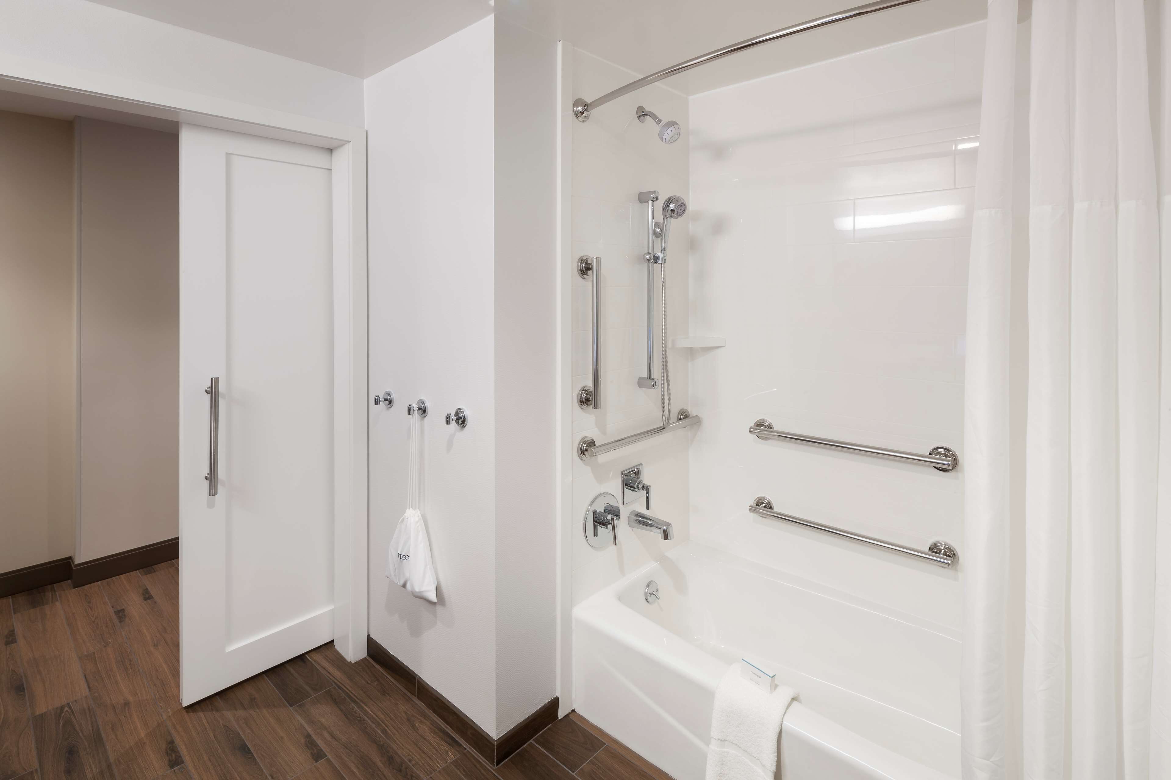 A modern bathroom with a walk-in shower, grab bars, and a white bathtub.