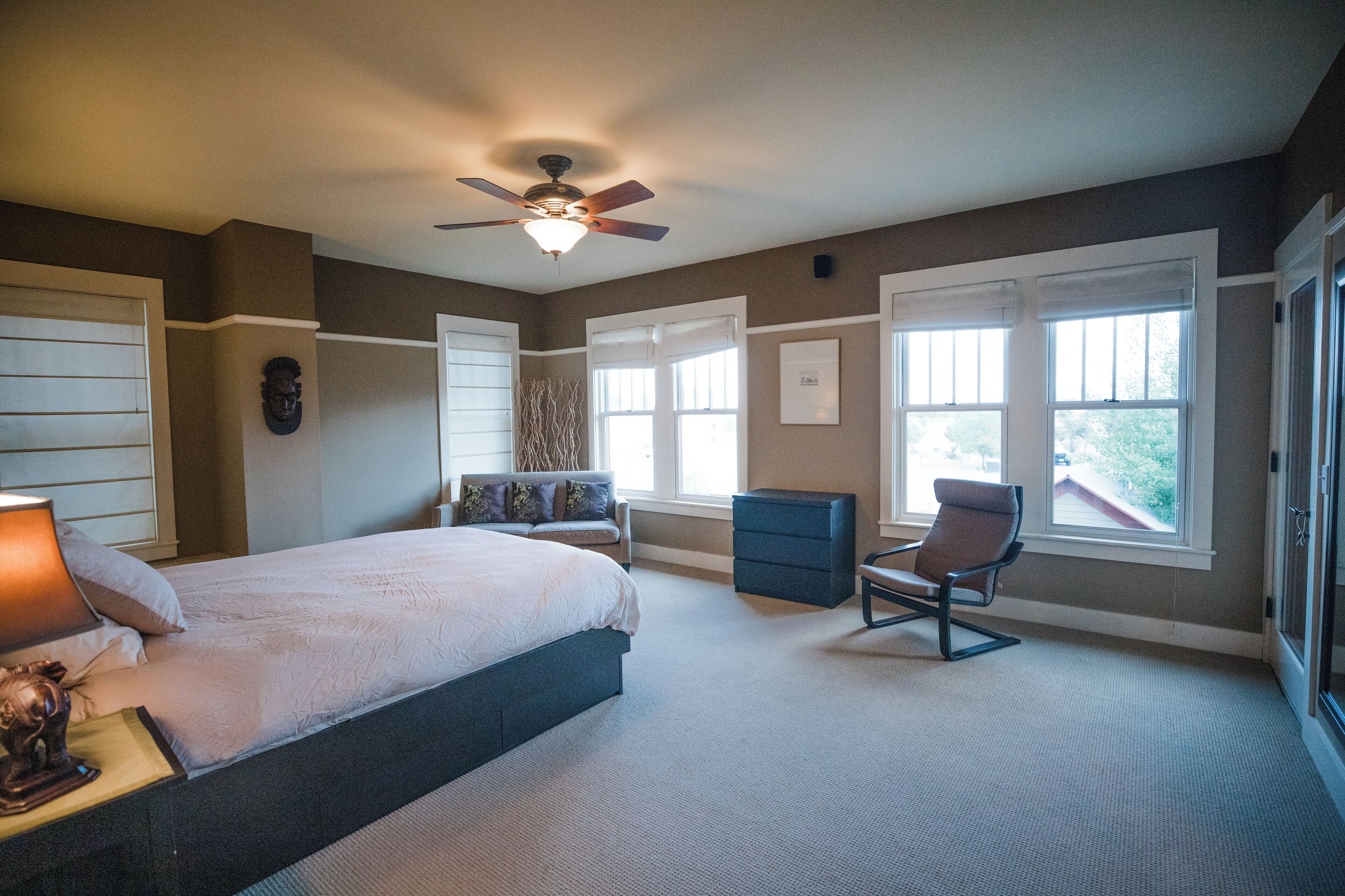 Quarto com cama, poltrona, mesa de cabeceira, cômoda e ventilador de teto.