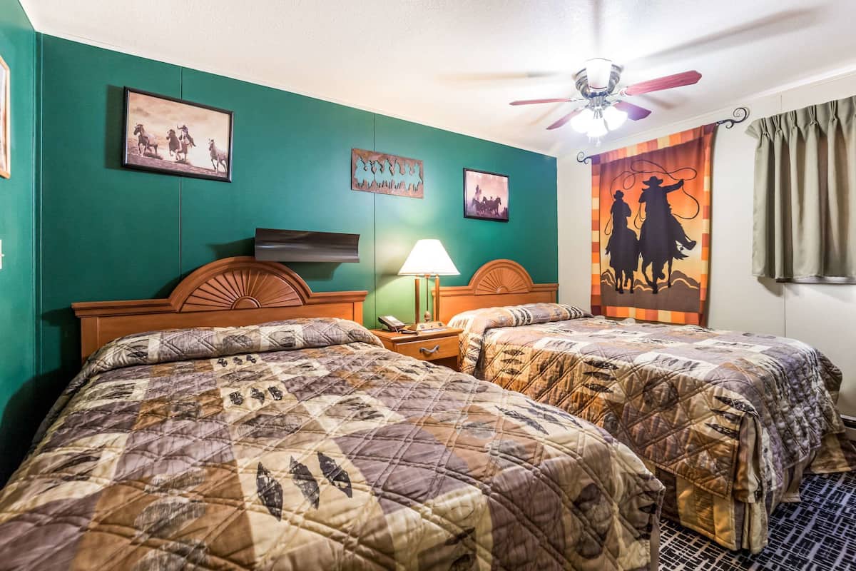 A hotel room with two beds, a ceiling fan, and artwork on the walls.