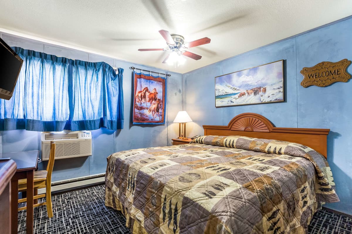A bedroom with a bed, a desk, a chair, a ceiling fan, a wall-mounted air conditioner, a window with curtains, and a welcome sign.