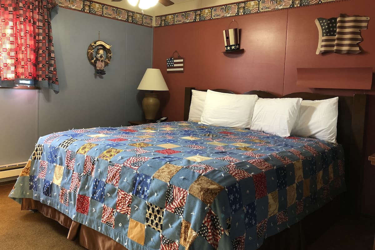 A bedroom with a bed, a ceiling fan, a lamp, and a wall with American flag decorations.