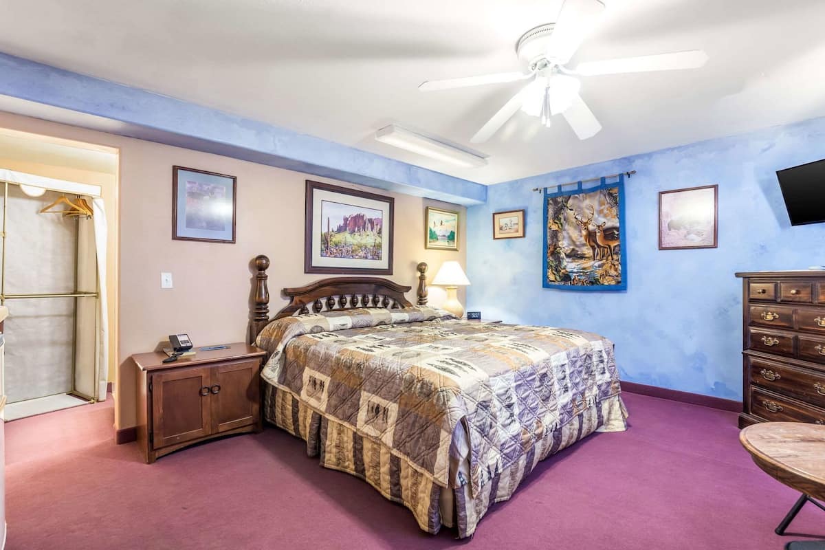 A bedroom with a bed, a dresser, a nightstand, a ceiling fan, and artwork on the walls.