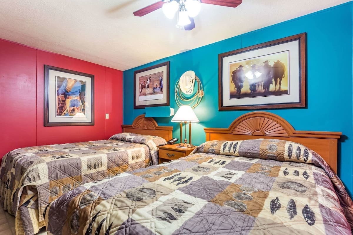 A room with two beds, a ceiling fan, and framed pictures on the walls.
