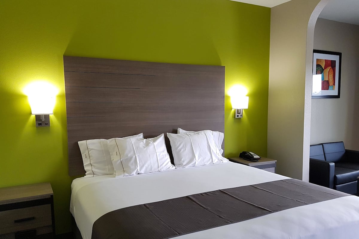Une chambre d’hôtel avec un lit, deux tables de chevet, une petite table, une chaise et un tableau au mur.