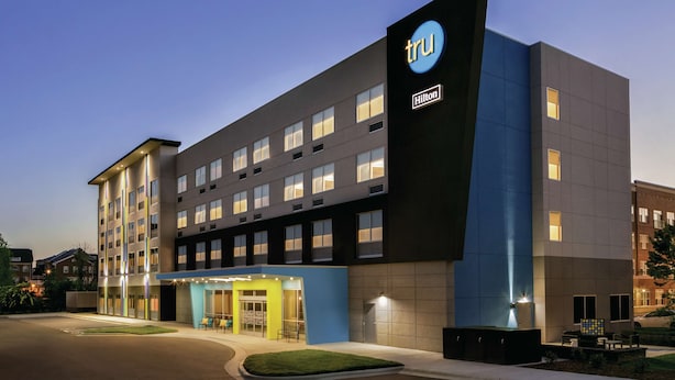 A modern hotel with a prominent TruHilton sign, multiple floors, and a well-lit entrance.
