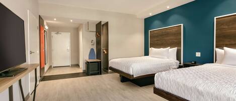A modern hotel room with two beds, a desk, and a TV.