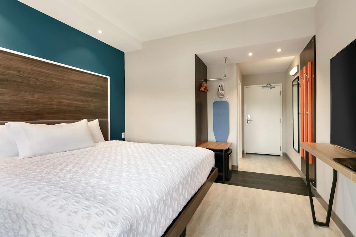 Una habitación de hotel moderna con una cama grande, un cabecero de madera, una mesita pequeña y un espejo.