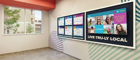 Un hall de hotel con una gran pantalla digital que anuncia atracciones locales y el lema 'LIVE TRULY LOCAL'.