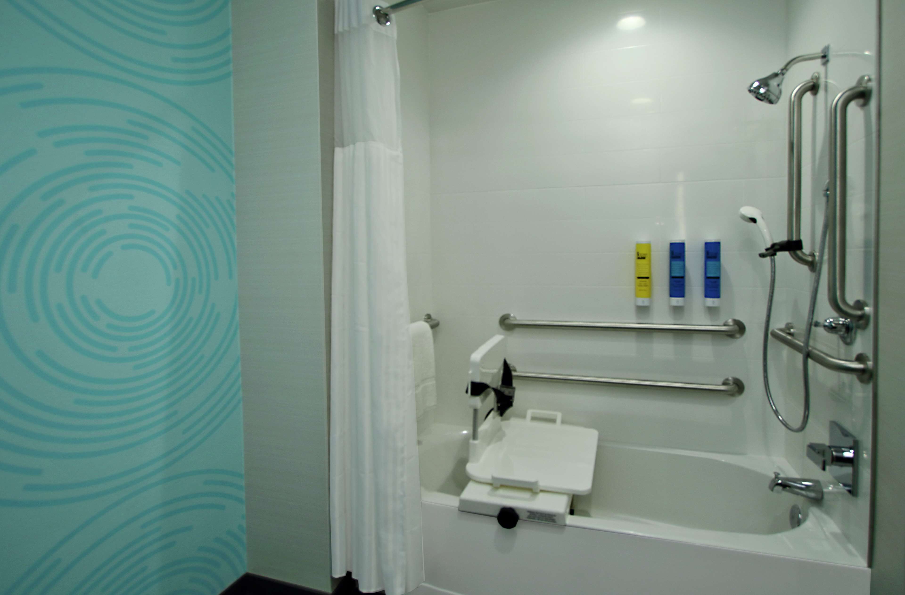 Un baño moderno con ducha a ras de suelo, barras de apoyo y un lavamanos blanco.