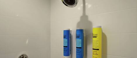 A shower area with a handheld showerhead and three soap dispensers on the wall.