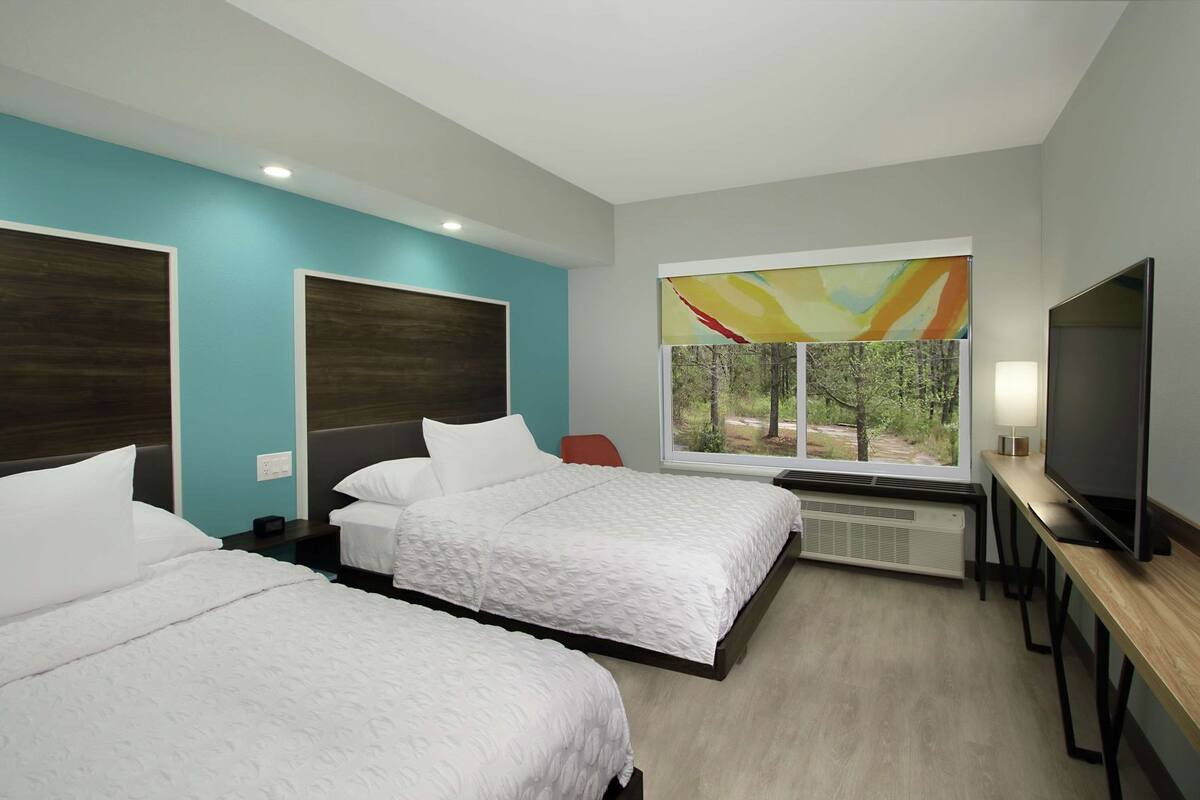 A hotel room with two beds, a TV, a window with a view, and a desk with a lamp.