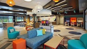 A modern hotel lobby with a blue sofa, orange ottoman, and a coffee bar.