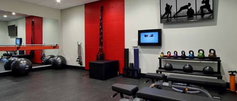 Une salle de sport équipée de matériel d’exercice, avec un mur rouge et un écran de télévision.
