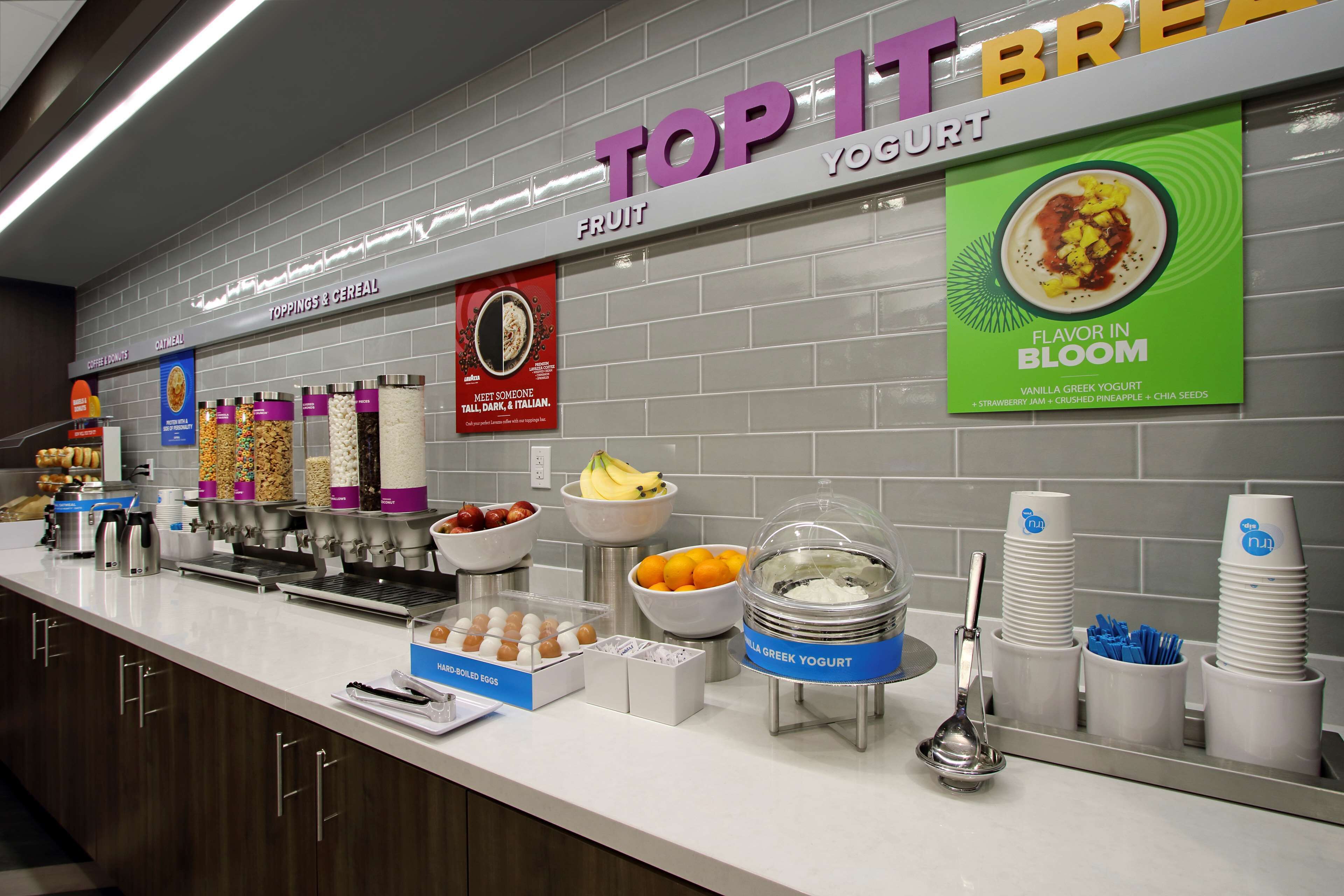 A breakfast buffet area with various food options, including yogurt, cereal, and fruit.