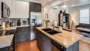 Een moderne keuken met een centraal eiland, roestvrijstalen apparatuur en een zithoek met een bank en lamp.