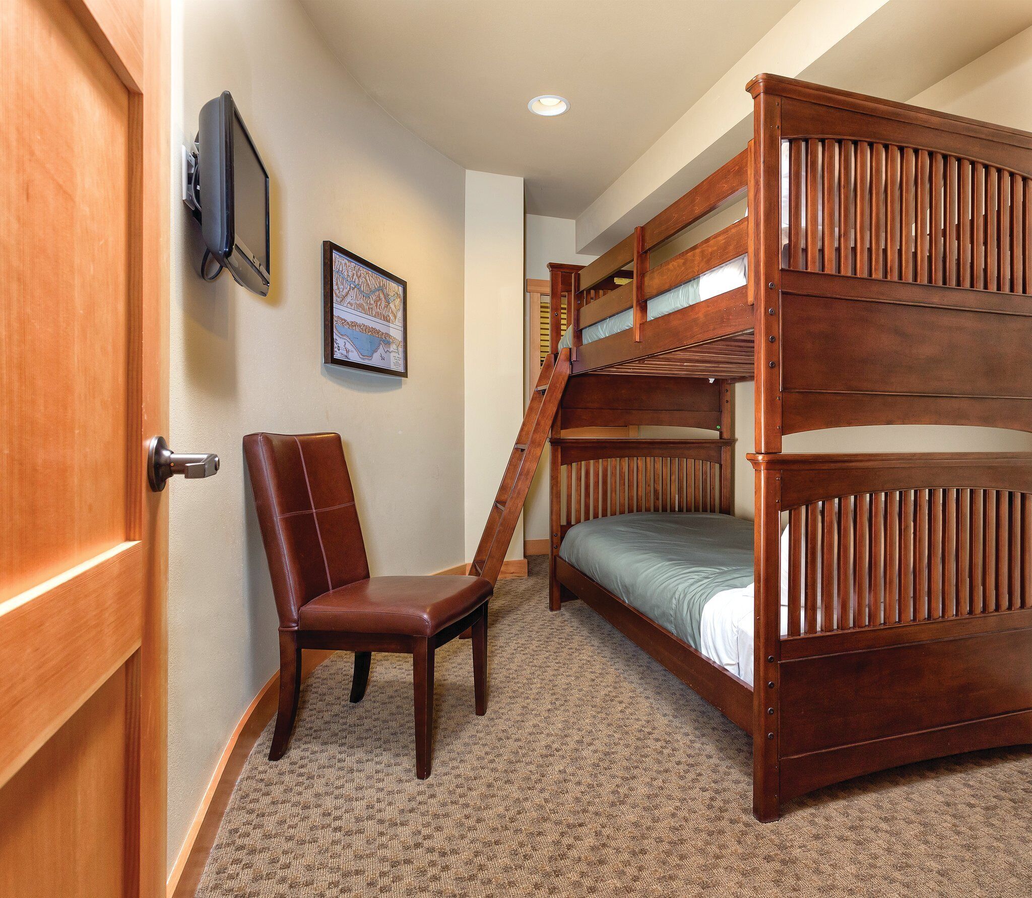 A room with a bunk bed, a chair, a door, and a framed map on the wall.