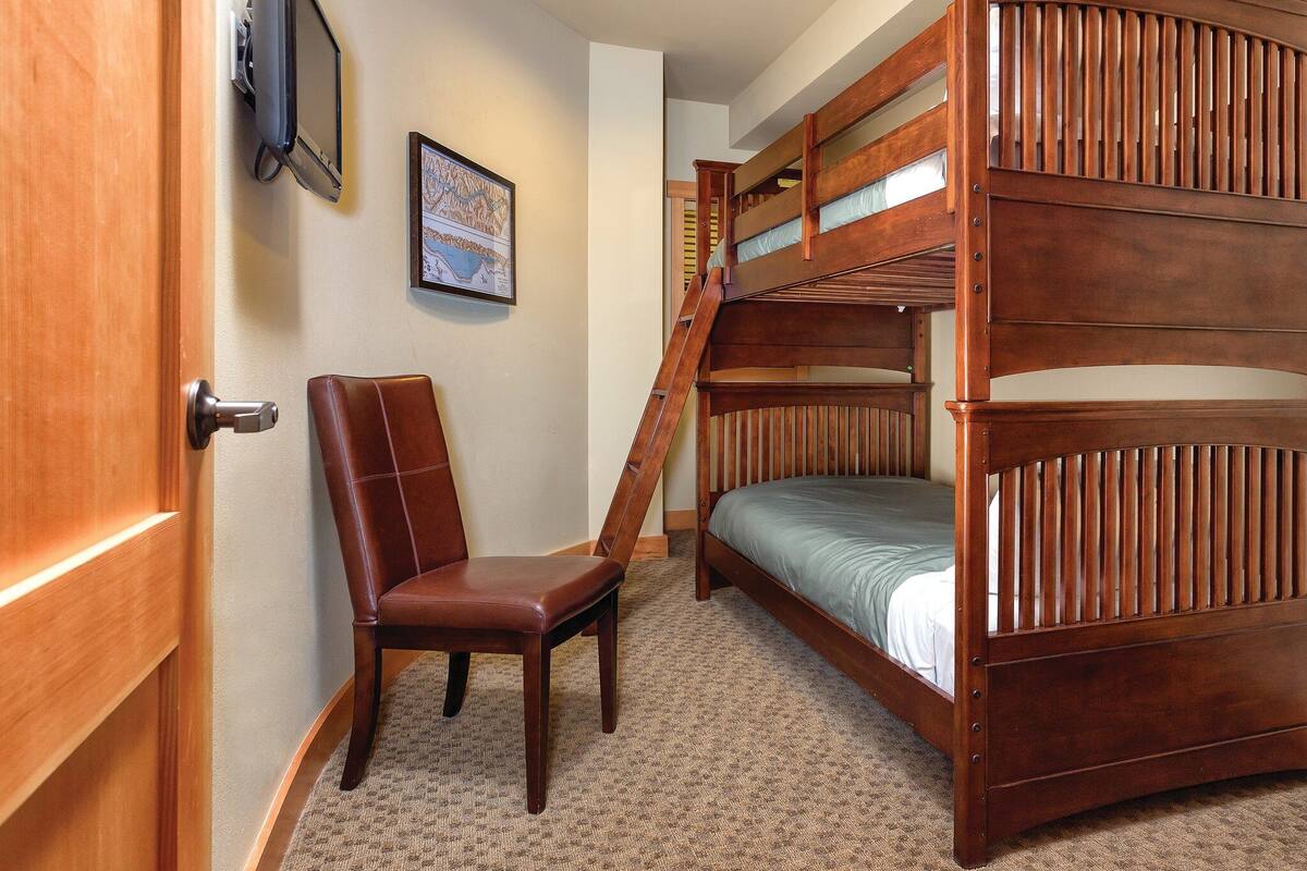 A room with a bunk bed, a chair, a door, and a framed map on the wall.