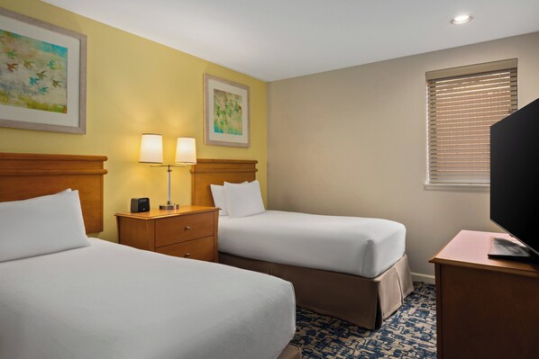 A hotel room with two beds, a desk, a TV, and artwork on the walls.