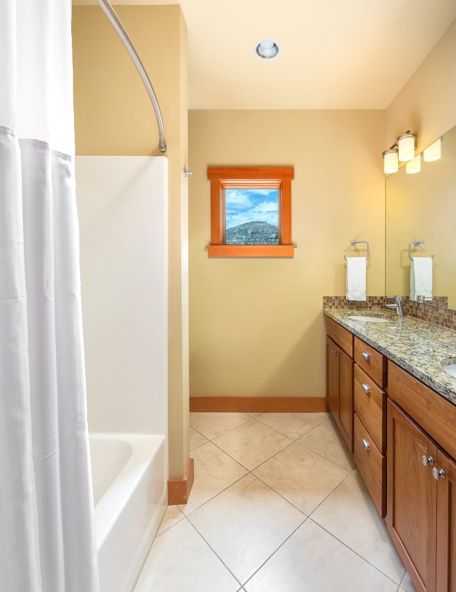 A bathroom with a bathtub, a window with a view of a hill, and a vanity with a mirror and sink.