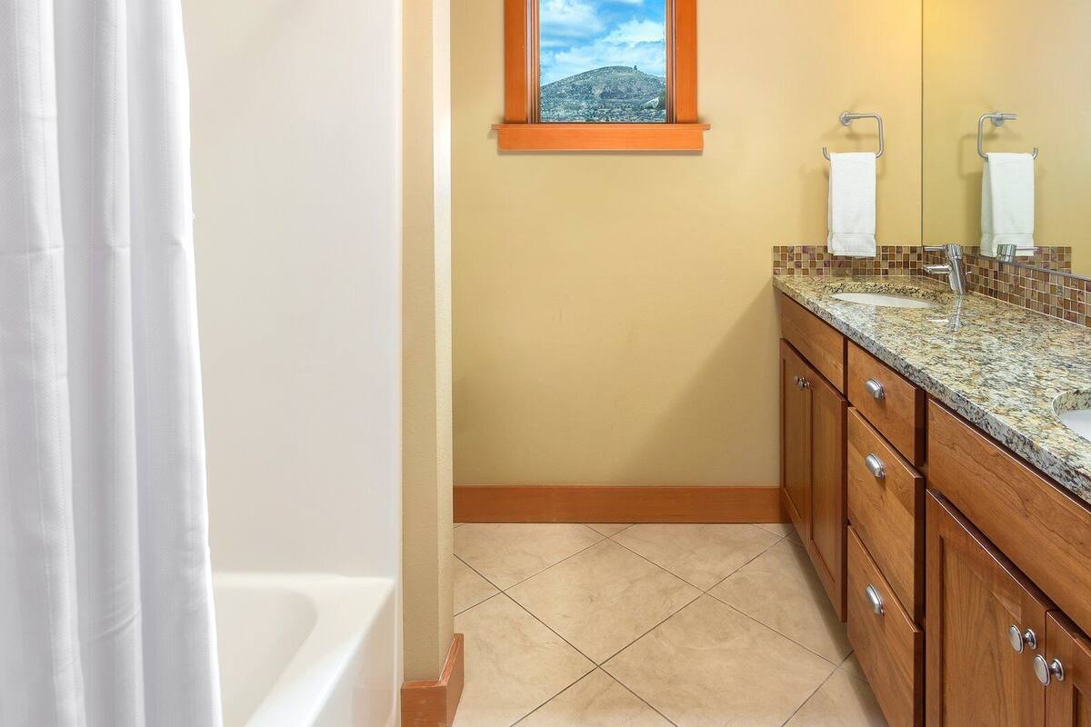 A bathroom with a bathtub, a window with a view of a hill, and a vanity with a mirror and sink.