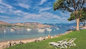 A lakeside view with boats, a tree, and two lounge chairs on a grassy area. - WorldMark Lake Chelan Shores (Chelan)