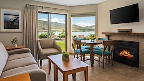 A living room with a sofa, chairs, a table, a fireplace, a TV, and a large window with a view of hills and water. - WorldMark Lake Chelan Shores (Chelan)