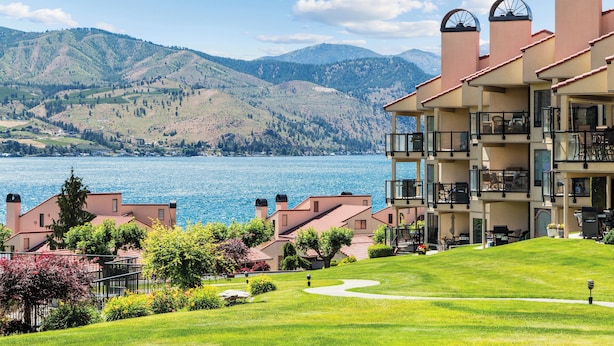 A hotel with a view of a lake and mountains. It has multiple floors with balconies and a well-maintained lawn. - WorldMark Lake Chelan Shores (Chelan)