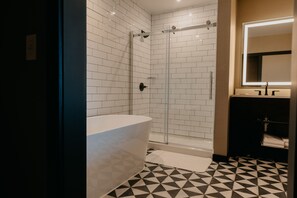 A modern bathroom with a white bathtub, a glass-enclosed shower, and a black and white tiled floor.