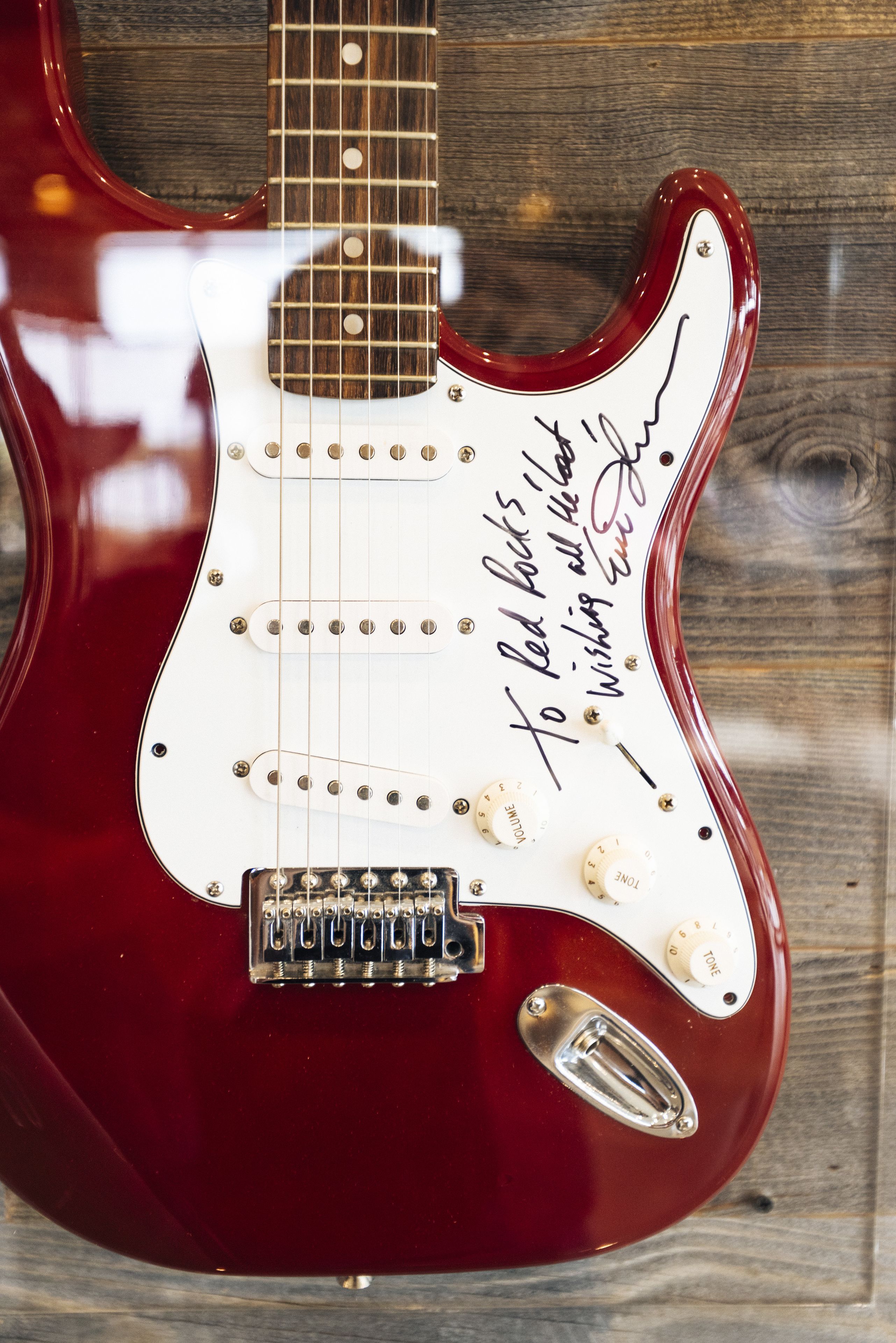Une guitare électrique rouge avec un protège-cordes blanc et une signature apposée sur le corps de l’instrument.
