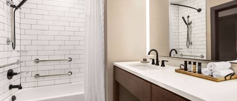A bathroom with a white-tiled shower, a wooden vanity with a mirror, and a black and white checkered floor.