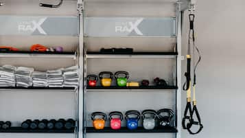 Ein Fitnessstudio mit gekennzeichneten Racks für Kettlebells und Kurzhanteln, sowie einem an der Wand montierten Trainingsgerät.