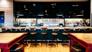 Un bar con taburetes de madera, una barra con diferentes botellas e iluminación colgante.