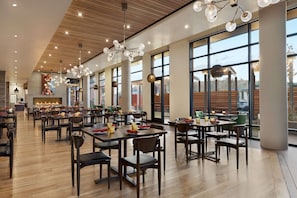 A spacious dining area with multiple tables and chairs, large windows, and a central fireplace.