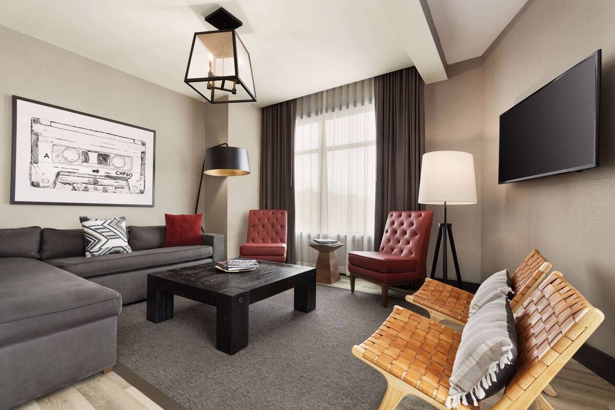 A modern living room with a sofa, armchair, and a coffee table. There is a television mounted on the wall and a framed picture on the wall.