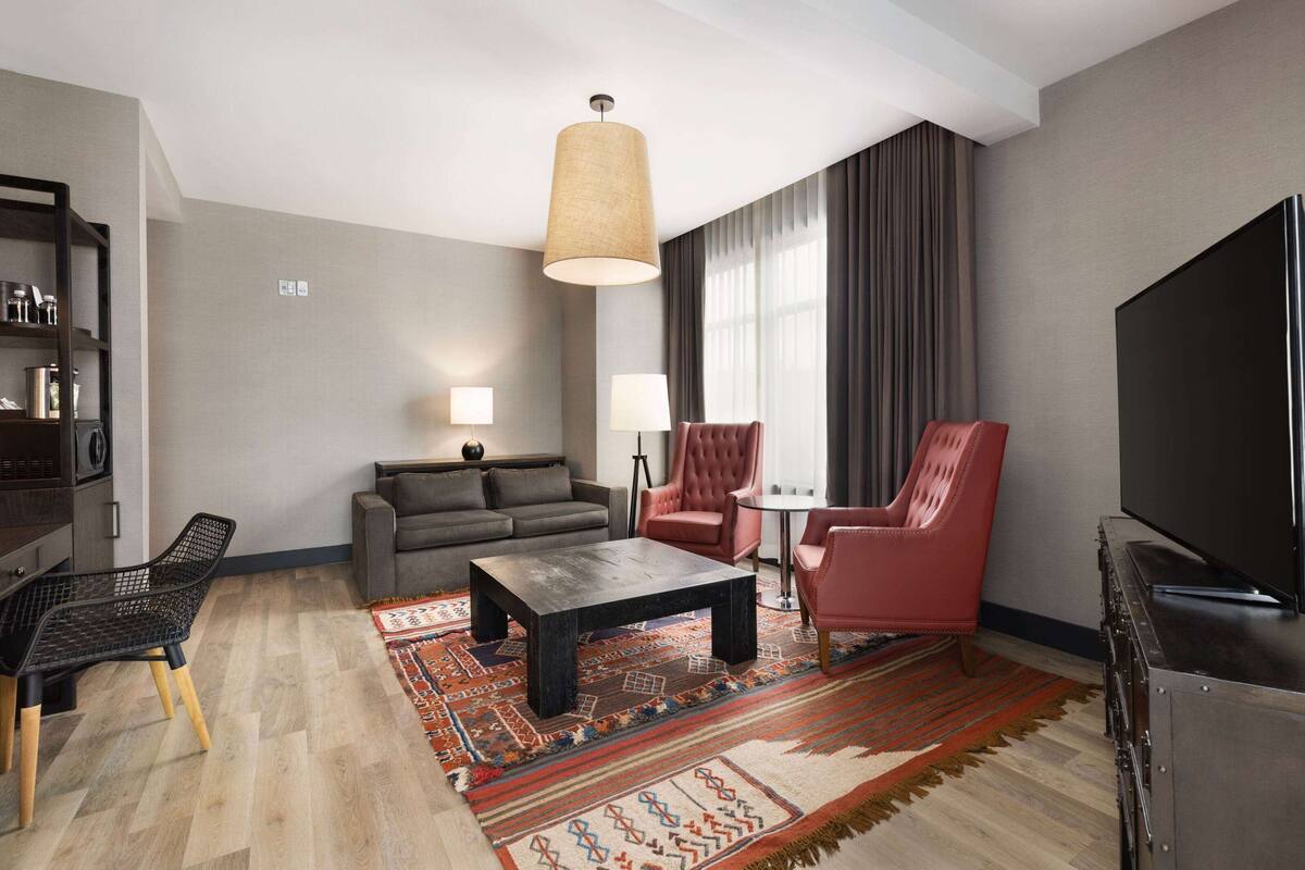 A modern living room with a sofa, two armchairs, a coffee table, a TV, and a bookshelf.