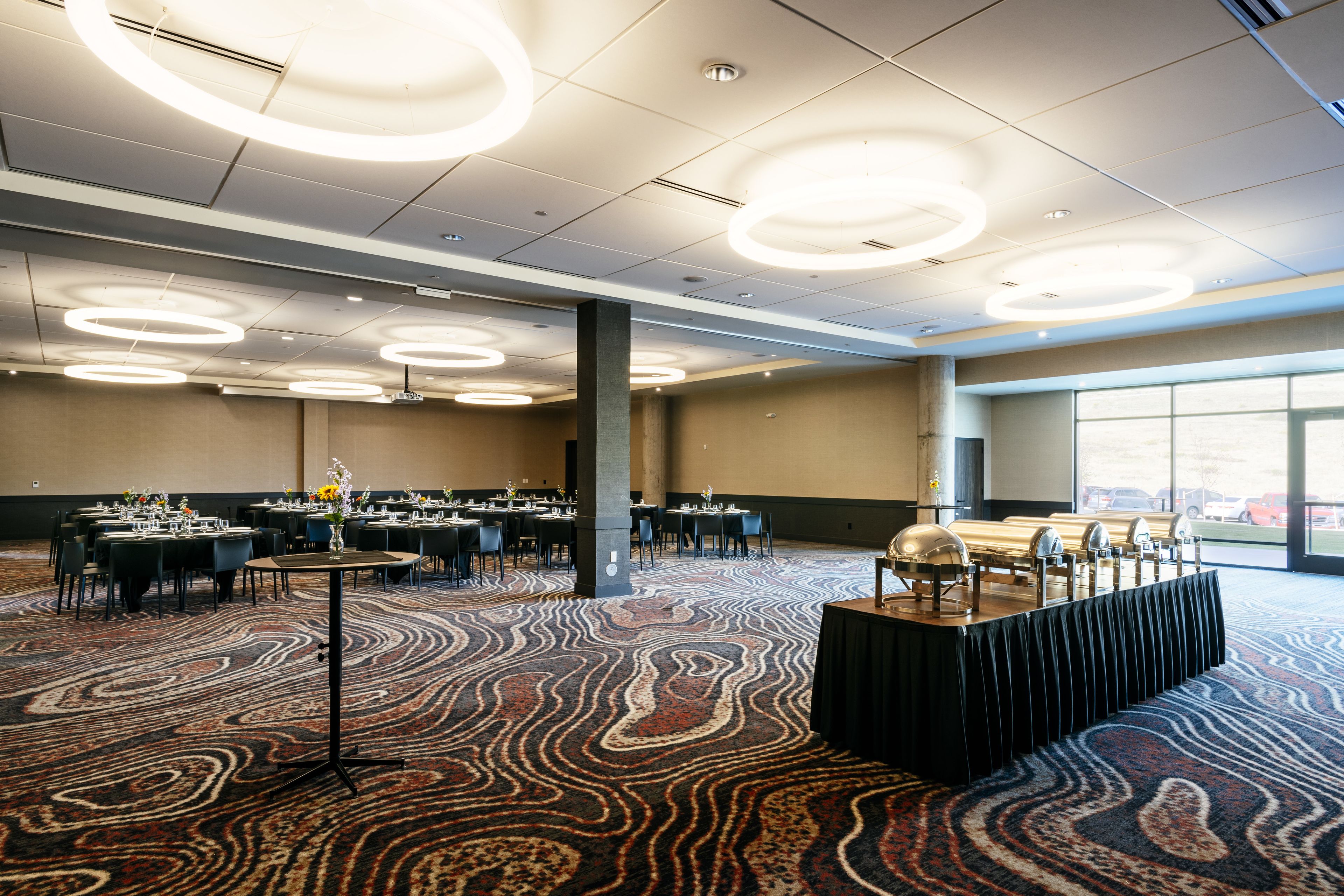 Une salle de banquet spacieuse, avec des tables rondes, une scène centrale et une grande fenêtre donnant sur la ville.