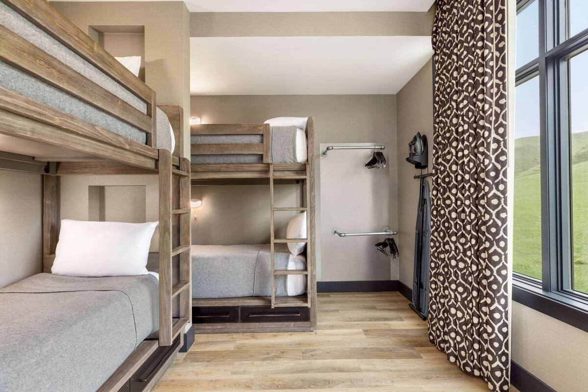 A compact room with a bunk bed, a small sofa, a ladder, a towel rack, and a window with patterned curtains.
