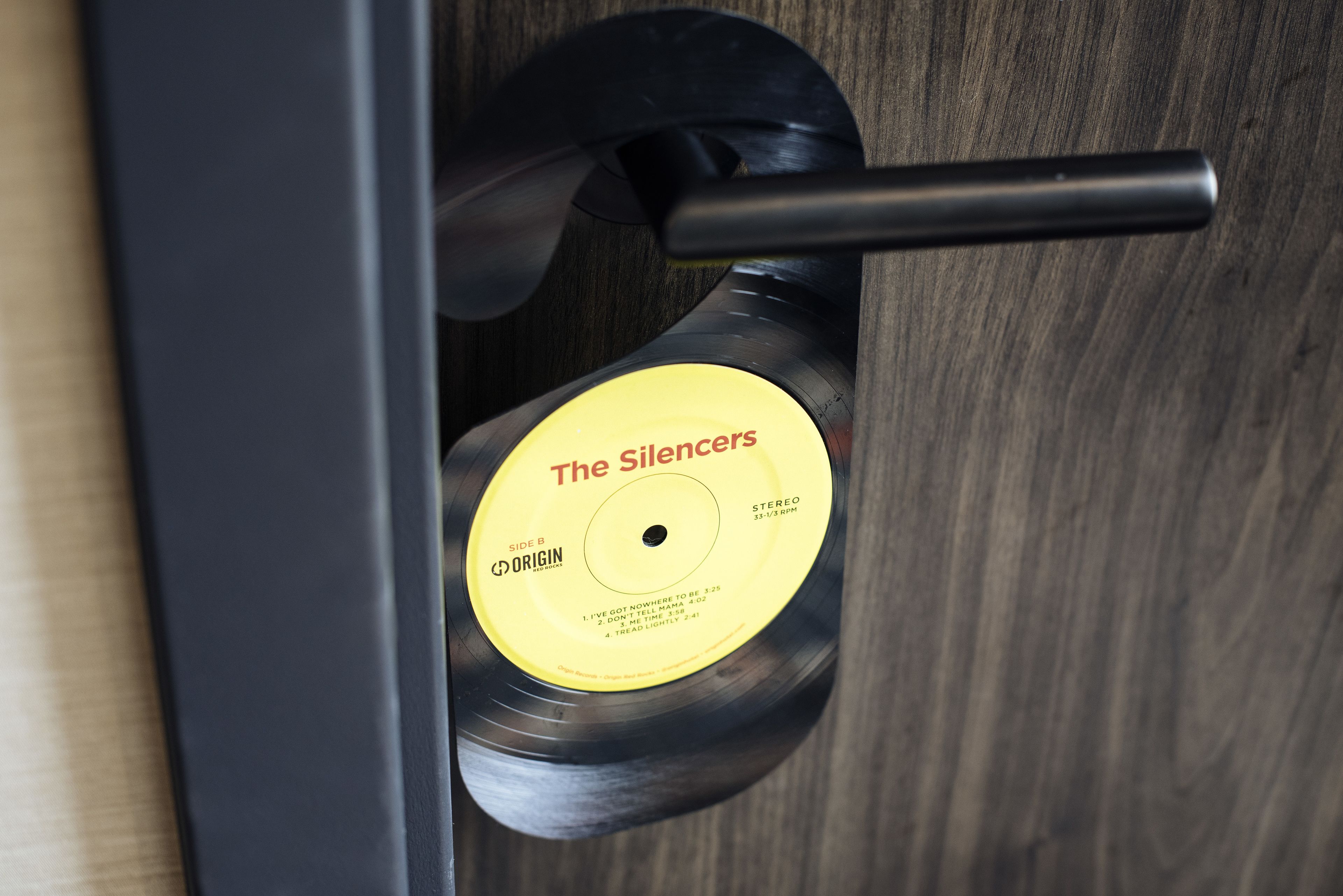 A vinyl record with the label "The Silencers" by ORIGIN, placed on a wooden surface.