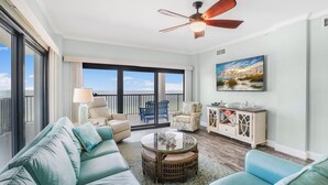 A spacious living room with a large sofa, a round coffee table, and a ceiling fan. There is a balcony with a view of the ocean. - Breathtaking Views, Views, Views! Oceanfront wraparound balcony; 3 BR and 3 BA. (Orange Beach)