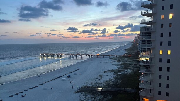 A beach with a pier extending into the ocean, a hotel with balconies overlooking the beach, and a pool area with sun loungers. - Breathtaking Views, Views, Views! Oceanfront wraparound balcony; 3 BR and 3 BA. (Orange Beach)