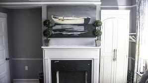 A room with a fireplace, a painting of a boat, and a white door. - Suites on Cannon (Charleston)