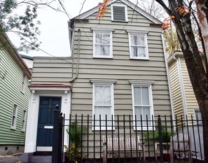 A two-story house with a black front door, white window shutters, and a black metal fence. - Suites on Cannon (Charleston)