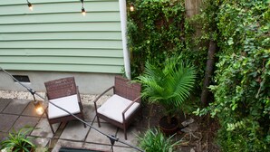 An outdoor patio with wicker furniture, a potted palm tree, and string lights. - Suites on Cannon (Charleston)