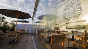 Een buitenruimte met eethoek, tafels, stoelen, parasols en een glazen wand met een decoratief ontwerp.