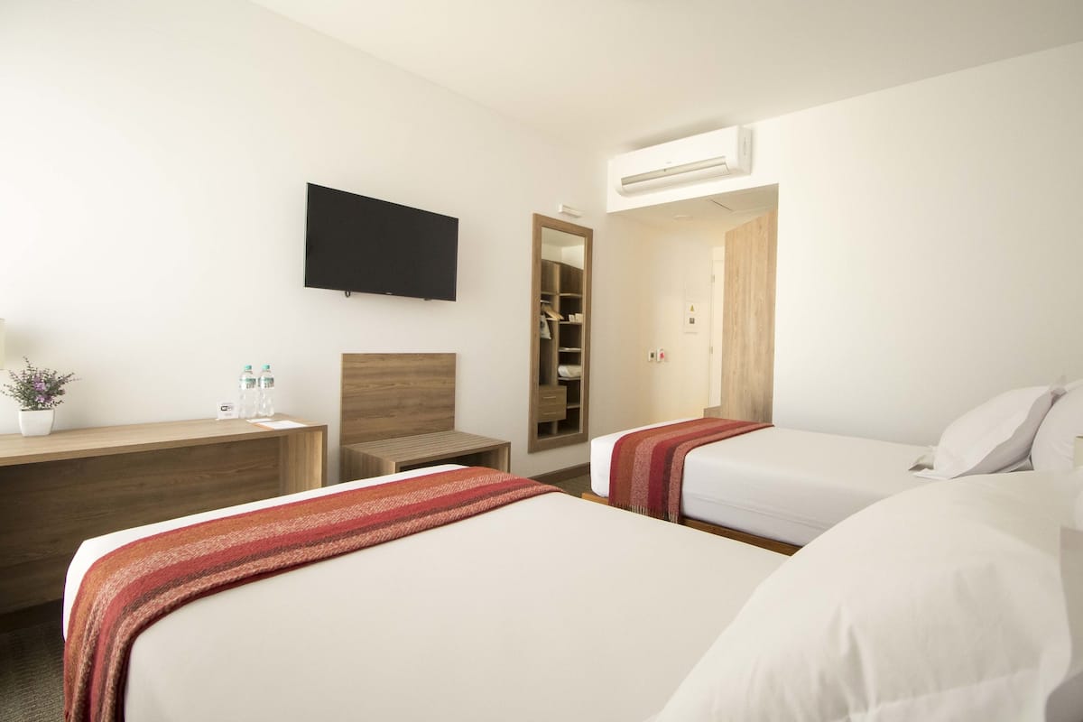 Ein Hotelzimmer mit zwei Betten, einem Schreibtisch, einem Fernseher und einem Kleiderschrank.