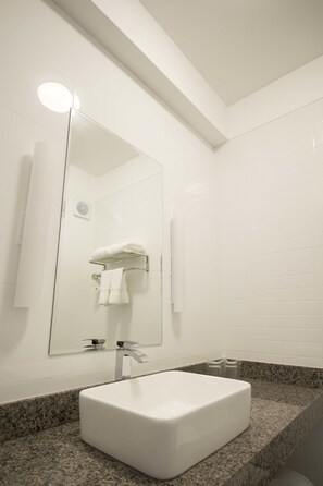 Une salle de bain moderne avec un lavabo blanc, un comptoir en granit et un grand miroir.